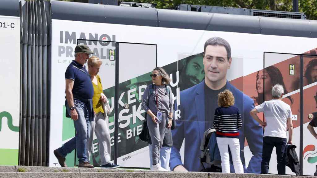 Ciudadanos pasan por delante de un tranvía con publicidad electoral del candidato del PNV a lehendakari, Imanol Pradales / Luis Tejido - EFE